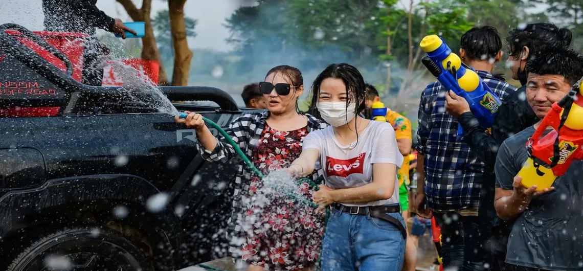 People spraying water and enjoying the Songkran Water Festival in Thailand with water guns and laughter.
