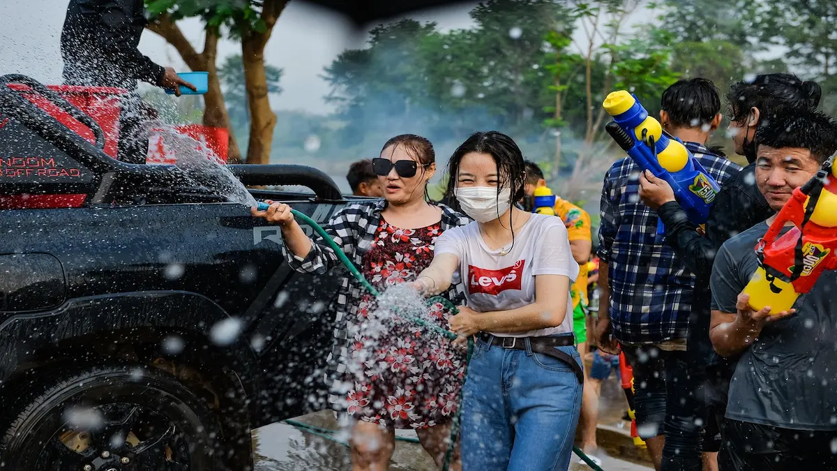 People spraying water and enjoying the Songkran Water Festival in Thailand with water guns and laughter.