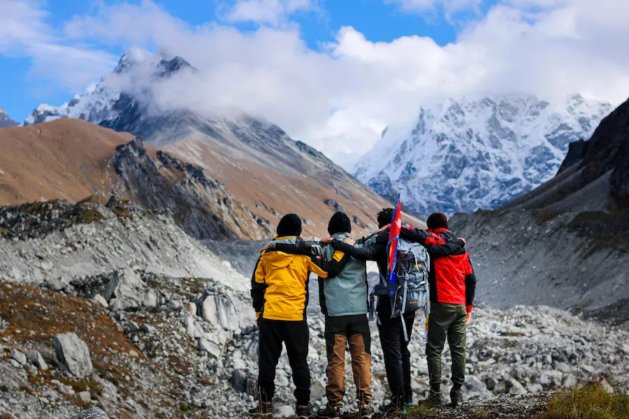 Four hikers with arms around each other facing snow-capped mountains in Nepal, holding a Nepalese flag — symbolizing small group travel and connection and team spirit with Resurgence Travel.