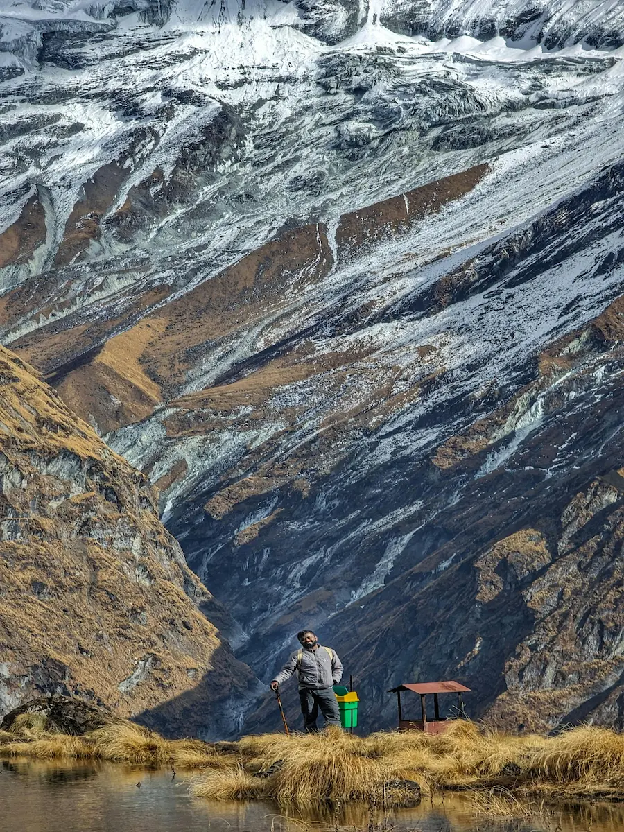 Trekker with backpack and trekking pole near a tarn below snow-streaked Himalayan slopes in Nepal