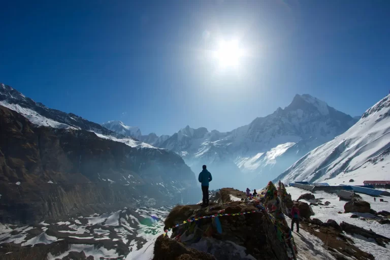 Trekker standing below the Annapurna mountain range in Nepal with prayer flags and snow-covered peaks.