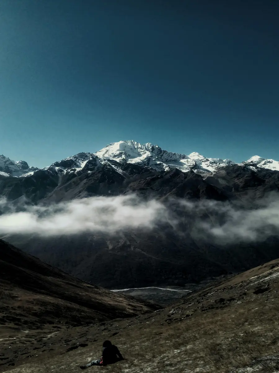 Hiker resting on a grassy slope with cloud inversion and snow-capped Himalayan peak in Nepal