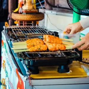 Hands turning skewers on a street grill at a Patong night market; sizzling, made-to-order street food.